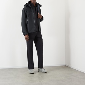 Model wearing black hooded zip-up jacket with black trousers and grey trainers, full-length view