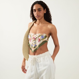 Model wearing Farm Rio Strilitzia Printed Handkerchief Bikini Top in Light Blush with botanical print and stripe trims, styled with white trousers