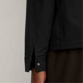 Reiss black long-sleeve top close-up showing cuff detail with silver button fastening, styled with dark brown trousers.
