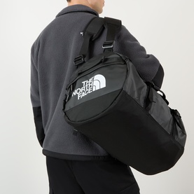 Model carrying North Face Base Camp Logo Duffel Bag in black, worn as backpack, with white logo branding visible on front panel
