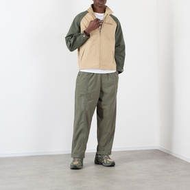 Model wearing Pleasures beige casual jacket with contrast khaki sleeves, styled with matching olive trousers and chunky trainers