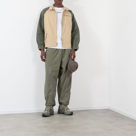 Model wearing Pleasures beige casual jacket with olive green sleeves, styled with matching olive trousers, bucket hat and hiking shoes.