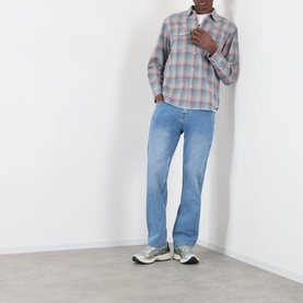 Model wearing Pleasures pink plaid cotton casual shirt, styled with light blue jeans and grey trainers