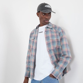 Model wearing Pleasures pink check cotton casual shirt, styled with white graphic tee and grey logo cap