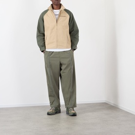 Model wearing Pleasures Sound Logo Track Pants in Olive, tapered leg with piping detail, styled with a two-tone fleece jacket and trail shoes.
