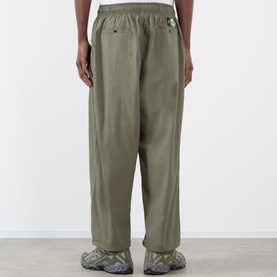 Model wearing Pleasures Sound Logo Track Pants in olive, showing rear view with elasticated waistband and tapered leg, styled with chunky trainers.