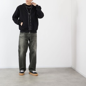 Model wearing Pleasures black cotton hoodie with stud detailing, styled with dark wash jeans and white platform trainers