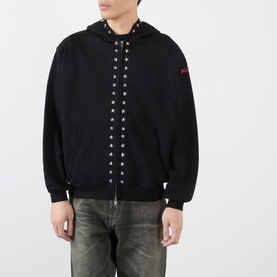 Model wearing Pleasures black cotton hoodie with silver eyelet lace detail down front zip, red logo patch on sleeve