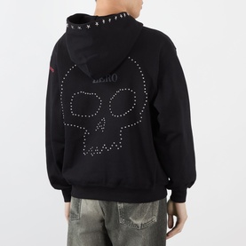 Model wearing Pleasures black cotton hoodie, back view, studded skull graphic, spiked neckline detail, styled with distressed jeans.