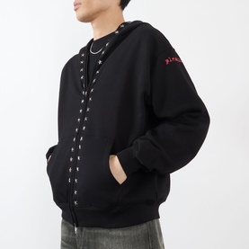 Model wearing Pleasures black cotton hoodie with silver eyelet lace-up front detail and red logo embroidery, styled with a chain necklace