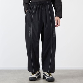 Model wearing Pleasures black nylon casual trousers with contrast piping and elasticated waist, styled with chunky trainers.