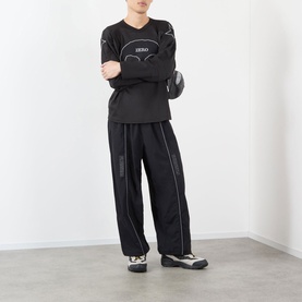 Model wearing Pleasures black nylon casual trousers with white contrast stitching, styled with a black long-sleeve top and white trainers.
