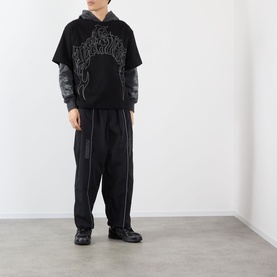 Model wearing Pleasures black cotton hoodie with flame graphic, styled with grey long-sleeve top, black wide-leg trousers and boots