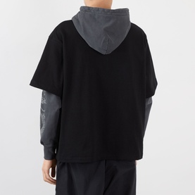 Model wearing Pleasures black cotton hoodie, shown from behind, with grey layered long-sleeve detail and black trousers.