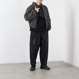 Model wearing Pleasures black cotton hoodie, styled with dark padded jacket, black tapered trousers and chunky black trainers