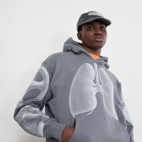 Model wearing Pleasures grey hoodie with chest lung graphic print and tonal mesh sleeves, styled with a black cap