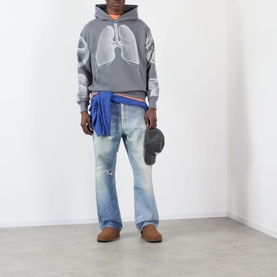 Model wearing Pleasures grey cotton hoodie with lung graphic print, styled with light wash distressed jeans, blue tied jacket and tan loafers