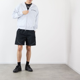 Model wearing Pleasures grey cotton hoodie with black shorts, white piping detail, black socks and chunky black trainers