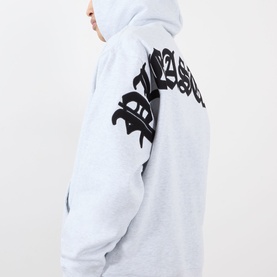 Model wearing Pleasures grey cotton hoodie with bold black gothic script graphic on sleeve and chest, hood up, side view