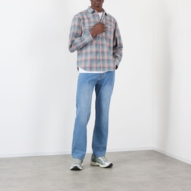 Model wearing Pleasures indigo straight-leg jeans with plaid overshirt, white tee and grey trainers