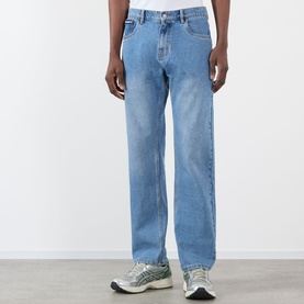 Model wearing Pleasures indigo straight-leg jeans in light wash cotton, styled with grey and silver chunky trainers