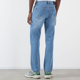 Model wearing Pleasures indigo straight-leg jeans, rear view, styled with green and white trainers.