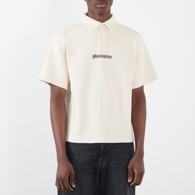 Model wearing Pleasures Cable Logo Polo Shirt in ecru, with polo collar, short sleeves, and chest logo, styled with dark jeans.