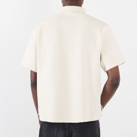 Model wearing Pleasures Cable Logo Polo Shirt in Ecru, back view showing dropped shoulders, short sleeves and straight hem in cable-knit texture.
