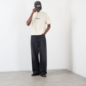 Model wearing Pleasures Cable Logo Polo Shirt in ecru with cable-knit texture, styled with dark wide-leg jeans and a black cap