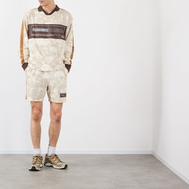 Model wearing Pleasures ecru camo-print shorts with matching long-sleeve top and chunky trainers