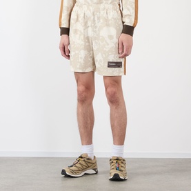 Model wearing Pleasures ecru floral-print shorts with logo patch, styled with a matching jacket and tan trail trainers.