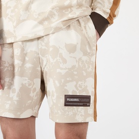 Model wearing Pleasures ecru floral camo print shorts with brown side stripe and branded patch label, paired with matching top.