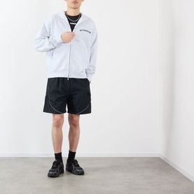 Model wearing Pleasures black nylon shorts with contrast piping detail, styled with a grey zip-up hoodie and black trainers.