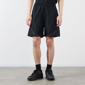 Model wearing Pleasures black nylon shorts with white piping detail, styled with black socks and grey chunky trainers.