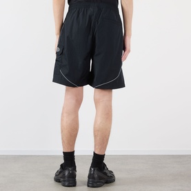 Model wearing Pleasures black nylon shorts with contrast piping and cargo pocket detail, styled with black socks and chunky black shoes.