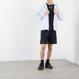 Model wearing Pleasures black nylon shorts with white contrast stitching, styled with a light blue zip-up hoodie, black tee and chunky trainers.