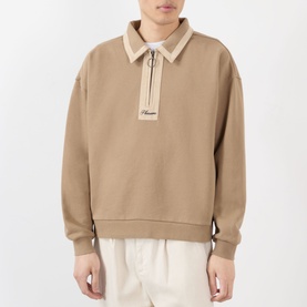 Model wearing Pleasures tan cotton quarter-zip sweatshirt with collar detail and small logo patch, styled with cream trousers