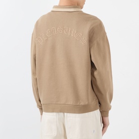 Model wearing Pleasures tan cotton sweatshirt, back view showing embroidered arc logo, ribbed cuffs and hem, styled with cream trousers