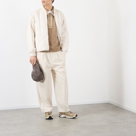 Model wearing Pleasures tan cotton sweatshirt with cream jacket, wide-leg trousers, and gold trainers