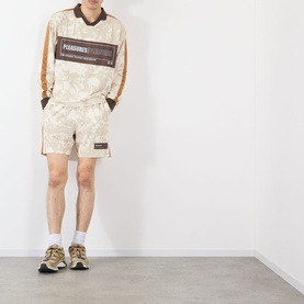 Model wearing Pleasures ecru cotton long-sleeve top with brown graphic print, styled with matching shorts and chunky trainers