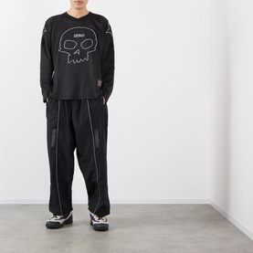 Model wearing Pleasures Jamie Hockey Jersey in black with skull graphic, styled with black wide-leg trousers and patterned trainers.