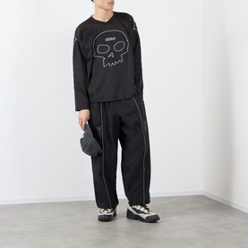 Model wearing Pleasures Jamie Hockey Jersey in black with skull graphic, styled with black contrast-stitch trousers and chunky trainers.