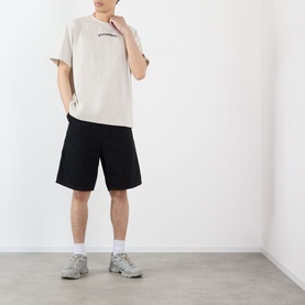Model wearing Pleasures oatmeal cotton T-shirt with logo print, styled with black shorts and grey trainers