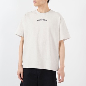 Model wearing Pleasures oatmeal cotton T-shirt with small arch logo print at chest, oversized fit, short sleeves.