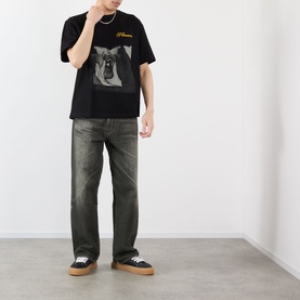 Model wearing Pleasures Ritual Graphic Print Logo T-Shirt in black with dark wash jeans and black low-top trainers with gum soles.