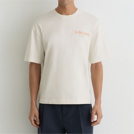 Model wearing Reiss white oversized crew neck T-shirt with orange chest logo print, styled with navy trousers.