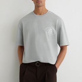 Model wearing Reiss powder blue oversized crew neck T-shirt with tonal chest logo, styled with dark brown trousers.