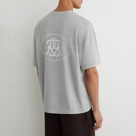 Model wearing Reiss powder blue oversized T-shirt, back view showing circular logo graphic print, styled with dark trousers.