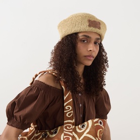 Model wearing Damson Madder Natural paper crochet beret with brown leather patch label, styled with a brown printed off-shoulder top.