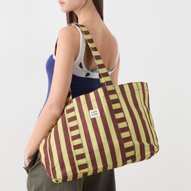 Model carrying Damson Madder Green Stripe cotton tote bag with bold burgundy stripes, single shoulder strap, and small logo patch.